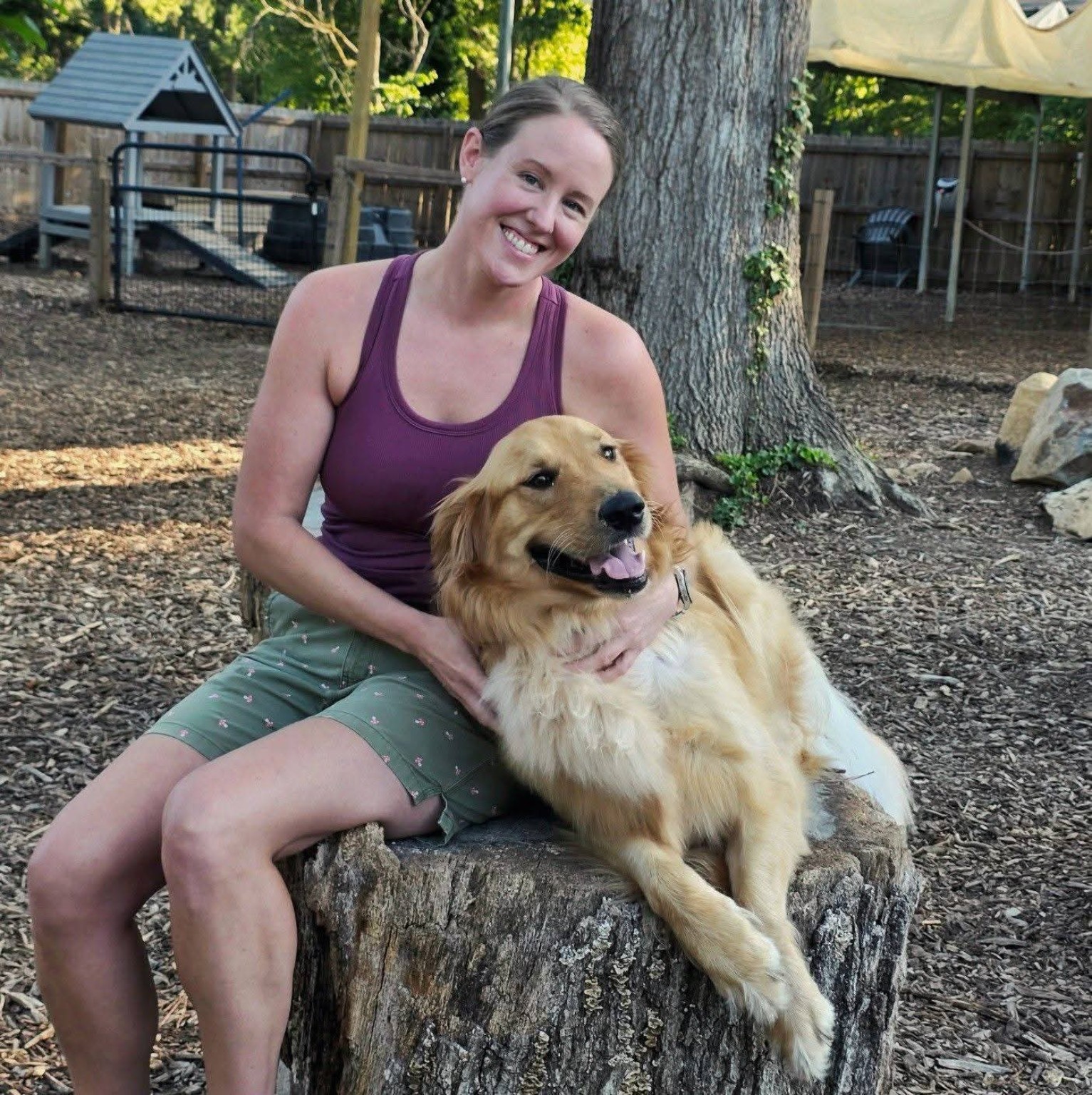 Casey Madden sitting with a golden retriever in the Rock Hill Pet Care yard